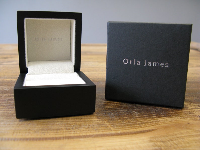 May include: A black square box with a white interior and the text "Orla James" on the lid. The box is open and the interior is visible.
