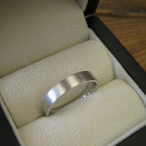 May include: A silver wedding band in a black ring box with a white velvet interior.
