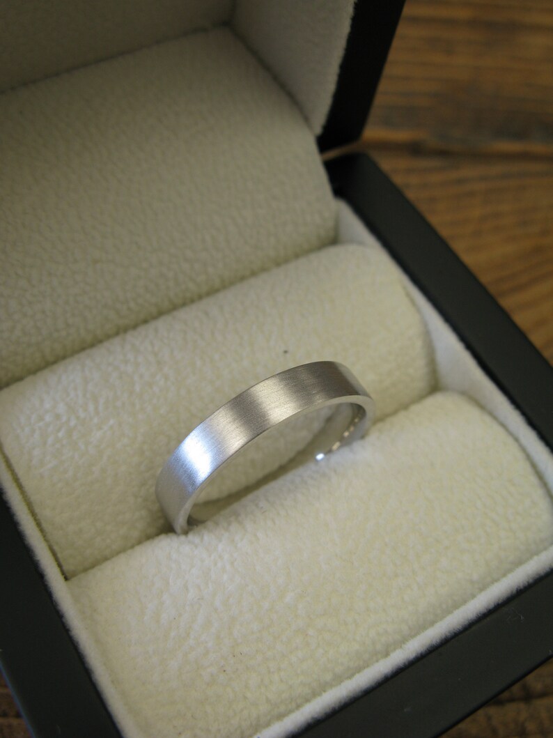 May include: A silver wedding band in a black ring box with a white velvet interior.
