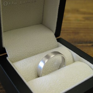 May include: A silver wedding band in a black ring box with a white interior. The box has the text "Orla James" on the lid.