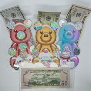 May include: Three clear plastic pockets with a $50 bill in each. Each pocket has a glittery cartoon teddy bear with a different color: pink, brown, and blue. The pink bear has a glittery heart, the brown bear has a candy jar, and the blue bear has a cupcake.