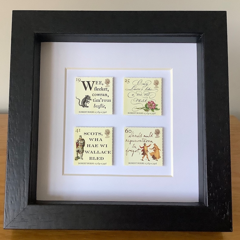 May include: Four framed stamps featuring quotes from Robert Burns, a Scottish poet. The stamps are in a black frame with a white mat. The stamps are arranged in a 2x2 grid. The top left stamp features a mouse and the text "Wee, fleeket, cowran, tim'rous beaftie". The top right stamp features a rose and the text "My Love's like a red, red Rose". The bottom left stamp features a knight and the text "Scots, Wha Hae Wi Wallace Bled". The bottom right stamp features a couple dancing and the text "Should auld acquaintance be forgot".