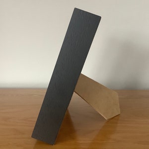 May include: A black wooden picture frame with a brown cardboard easel stand.