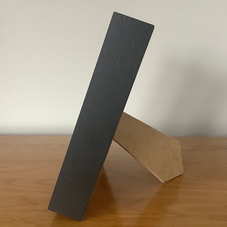 May include: A black wooden picture frame with a brown cardboard easel stand.
