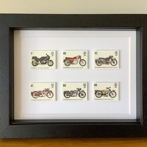 May include: A framed set of six vintage motorcycle stamps. The stamps feature different models of motorcycles, including a Triumph, a BSA, and a Norton. The stamps are in mint condition and are displayed in a black frame with a white mount.