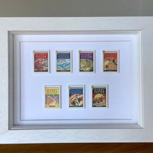 May include: A white frame with a white mount displays eight Harry Potter book cover stamps. The stamps are arranged in two rows of four. Each stamp features a different book cover illustration and the text "Harry Potter".