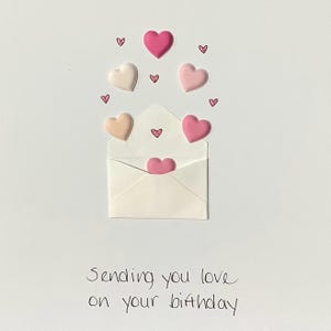 Puede incluir: Un sobre blanco con corazones rosas y melocot&oacute;n que salen de &eacute;l. El texto "Sending you love on your birthday" est&aacute; escrito debajo del sobre.