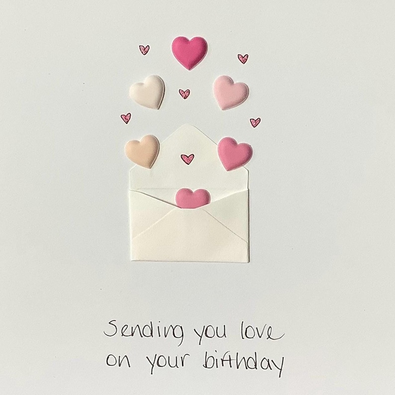 Puede incluir: Un sobre blanco con corazones rosas y melocot&oacute;n que salen de &eacute;l. El texto "Sending you love on your birthday" est&aacute; escrito debajo del sobre.