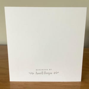 Puede incluir: Una tarjeta blanca con el texto "Handmade by Annie B Designs" en letras grises.