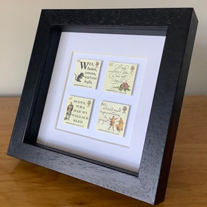 May include: A framed set of four vintage postage stamps featuring illustrations and text from the works of Robert Burns. The stamps are in a black frame with a white mat.