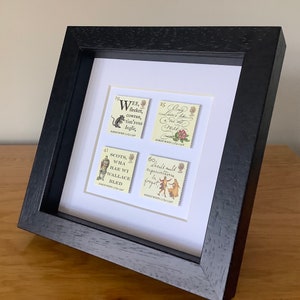 May include: A framed set of four vintage postage stamps featuring quotes from Robert Burns. The stamps are in a black frame with a white mat. The stamps feature the following quotes: "Wee, sleeket, cowran, tim'rous beastie," "Scots, wha hae wi Wallace bled," "Ony Lover's like a Red, Red Rose," and "Should auld acquaintance be forgot."