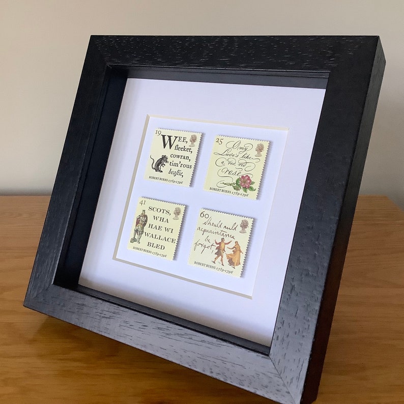 May include: A framed set of four vintage postage stamps featuring quotes from Robert Burns. The stamps are in a black frame with a white mat. The stamps feature the following quotes: "Wee, sleeket, cowran, tim'rous beastie," "Scots, wha hae wi Wallace bled," "Ony Lover's like a Red, Red Rose," and "Should auld acquaintance be forgot."