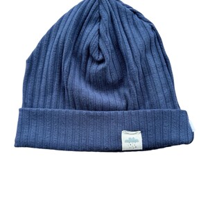 Könnte beinhalten: Eine marineblaue gerippte Mütze mit einem kleinen weißen Etikett, auf dem eine Wolke mit Regentropfen abgebildet ist.