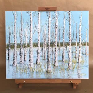 May include: A painting of a birch tree forest with a blue sky and white clouds. The trees are reflected in the water. The painting is on a wooden easel.