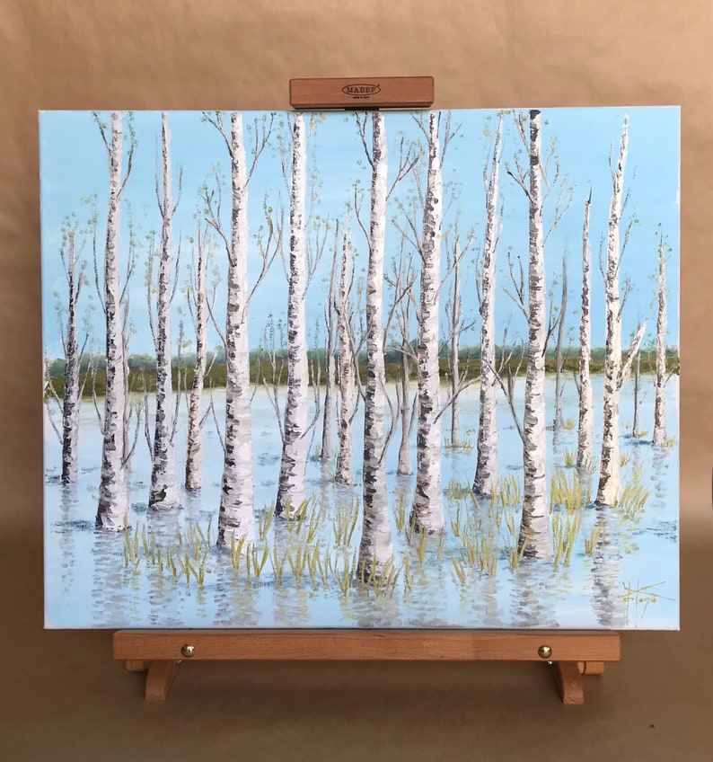 May include: A painting of a birch tree forest with a blue sky and white clouds. The trees are reflected in the water. The painting is on a wooden easel.