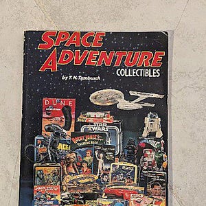 May include: A vintage book titled "SPACE ADVENTURE COLLECTIBLES" by T.H. Tumbusch. The cover features a dark blue background with red and yellow text, and images of various space-themed collectibles, including Star Wars and Dune.