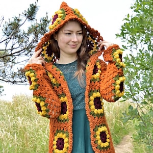 Peut inclure: Un long cardigan en crochet avec une capuche, orné d'un motif de tournesol dans des tons d'orange, jaune, vert et marron. Le cardigan est ouvert sur le devant et a une coupe ample.
