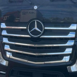 May include: Close-up of a black truck grille with chrome accents. The Mercedes-Benz logo is centered on the grille. The grille has horizontal chrome bars and a mesh pattern.
