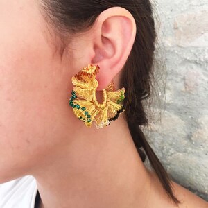 May include: Gold hoop earrings with a floral design featuring green, black, and brown beads.