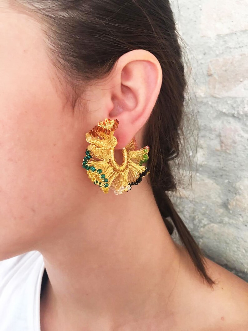 May include: Gold hoop earrings with a floral design featuring green, black, and brown beads.