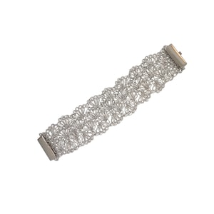 May include: A silver bracelet with a delicate, intricate design. The bracelet is made of a series of interconnected loops that create a delicate, airy look.