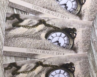 May include: Three cards with a vintage pocket watch resting on a sandy surface. Each card has the text "Timing Oracle Deck" printed on it.