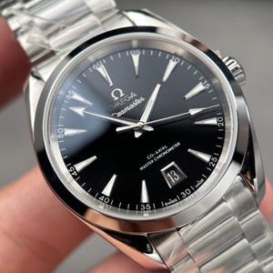 May include: An Omega Seamaster wristwatch with a black dial, silver-tone hands, and hour markers. The watch features a stainless steel case and bracelet, a date window at the six o'clock position, and text reading Omega Seamaster Co-Axial Master Chronometer.