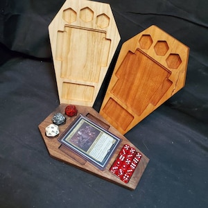 May include: Two wooden coffin-shaped dice trays, one stained a light brown and the other a dark brown. The dark brown tray has a card slot and is filled with red dice. The light brown tray has a compartment for dice.
