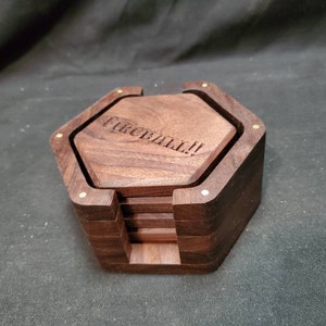 May include: A set of six hexagonal wooden coasters with a brass inlay. The top coaster has the words "FIREBALL!" engraved on it.