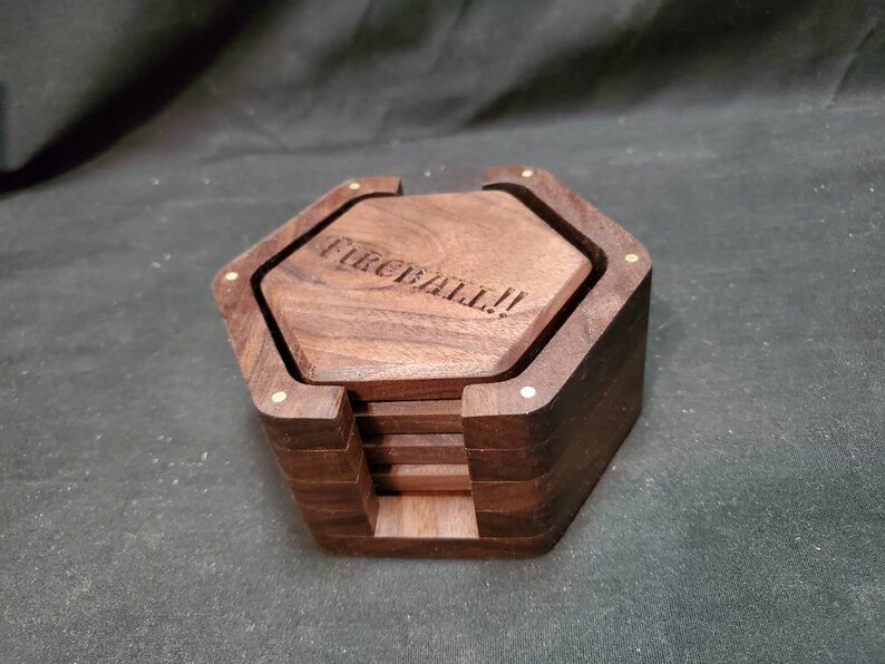 May include: A set of six hexagonal wooden coasters with a brass inlay. The top coaster has the words "FIREBALL!" engraved on it.