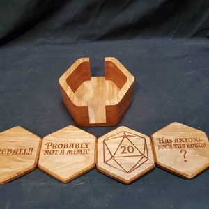 May include: Wooden hexagonal coasters with engraved text and a 20-sided die. The coasters feature phrases like "Fireball!" and "Probably not a mimic". The die is in the center of the coasters. The coasters are in a wooden holder.