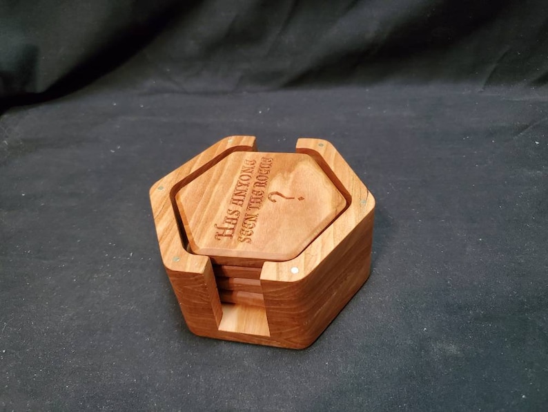 May include: A set of six wooden coasters in a hexagonal holder. The coasters are engraved with the text "Has anyone seen the booze?" and a question mark.