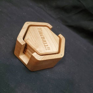 May include: Set of six hexagonal wooden coasters in a holder. The coasters are made of light wood and have the word "FIREBALL" engraved on the top. The holder is made of dark wood and has a hexagonal shape.