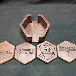 May include: Set of six wooden coasters with engraved designs. The coasters feature phrases like "Fireball!!", "Probably not a mimic", and "Has anyone seen the rogue?" One coaster has a 20-sided die design with the number 20 engraved on it. The coasters are made of dark wood and have a hexagonal shape.