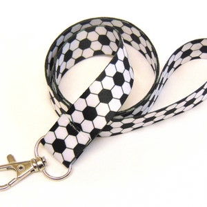 Op de afbeelding: Een zwart-witte lanyard met een voetbalpatroon en een zilveren draaibare clip.