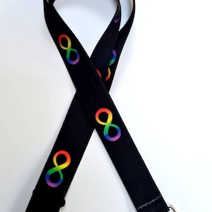 Puede incluir: Cordón negro con un patrón repetido de símbolos de infinito arcoíris. El cordón tiene un cierre de metal y una pieza ajustable de plástico negro. Los símbolos de infinito son de colores arcoíris.