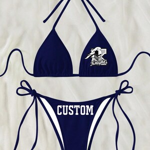 May include: Navy blue bikini with a white graphic of a knight's helmet and the word "Knights". The bottom of the bikini has the word "CUSTOM" printed in white.