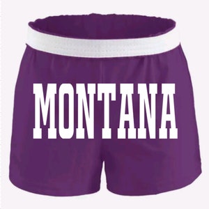 May include: Purple athletic shorts with a white waistband and the word "MONTANA" printed in white on the front.