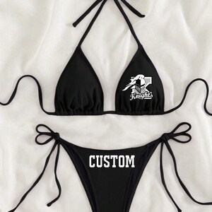 May include: Black bikini with a custom design. The top has a white knight logo with the text "Knights" and the bottom has the word "CUSTOM" printed in white.