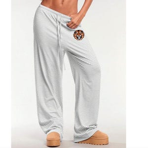 May include: White and gray striped pajama pants with a drawstring waist. The pants feature a tiger head logo on the left leg. The pants are made of a soft, lightweight material.