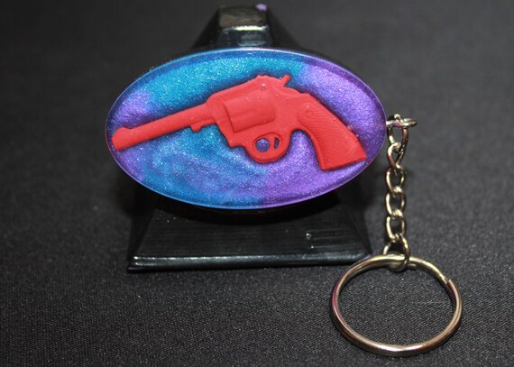 Pew Pew - Shoot em Up - Revolver in Red floating in a bed, Mica softly wraps glass EMF Blocker Keychain Pocket Electrical Blocker 2 inch