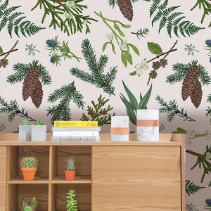 Puede incluir: Un papel tapiz rosa claro con un patrón repetitivo de ramas de pino verdes, piñas y otras plantas verdes. Un armario de madera con estantes está en primer plano, con libros y plantas en macetas en la parte superior.
