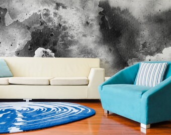 May include: A white sofa and a blue armchair with a striped pillow sit in front of a wall with a black and white abstract design.