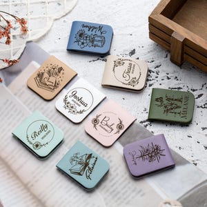 Puede incluir: Surtido de marcapáginas de cuero de colores con nombres personalizados y diseños florales. Cada marcapáginas presenta un diseño único con un nombre y un motivo floral. Los marcapáginas están hechos de cuero de alta calidad y son perfectos para los amantes de los libros.
