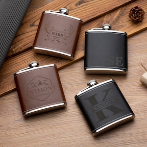 May include: Four personalized leather-wrapped hip flasks with engraved names and designs. The flasks are brown and black with silver accents. The designs include a stag, a mountain, and initials.