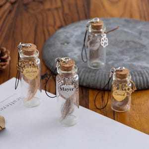 May include: Four small glass bottles with cork stoppers, each containing a sample of hair or fur. The bottles have decorative charms with names like "Jordan" and "Mayer". The bottles are on a wooden surface.