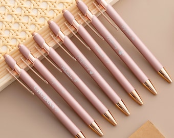 May include: Set of seven rose gold pens with gold accents and personalized names. Each pen has a different name engraved on it.