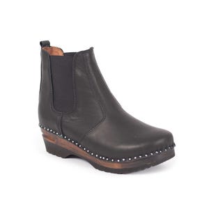 Può includere: Stivaletto alla caviglia in pelle nera con suola in legno e borchie color argento. Lo stivaletto ha la punta arrotondata, pannelli laterali elastici e un tacco a zeppa basso. Uno stile classico adatto a vari outfit.
