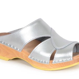 May include: Silver leather clog with a wooden platform sole and a peep toe. The clog has a strap across the top of the foot and a buckle closure.