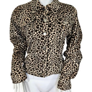 May include: A leopard print jacket with a collared neckline and button-down closure. The jacket features a classic design with two chest pockets and long sleeves. The animal print is in shades of tan, brown, and black.